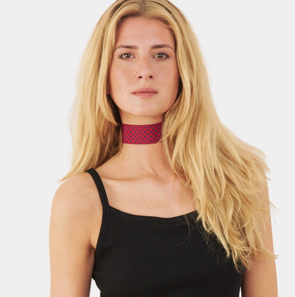 model wearing a scarlet red silk choker with a repeating blue polka dot pattern